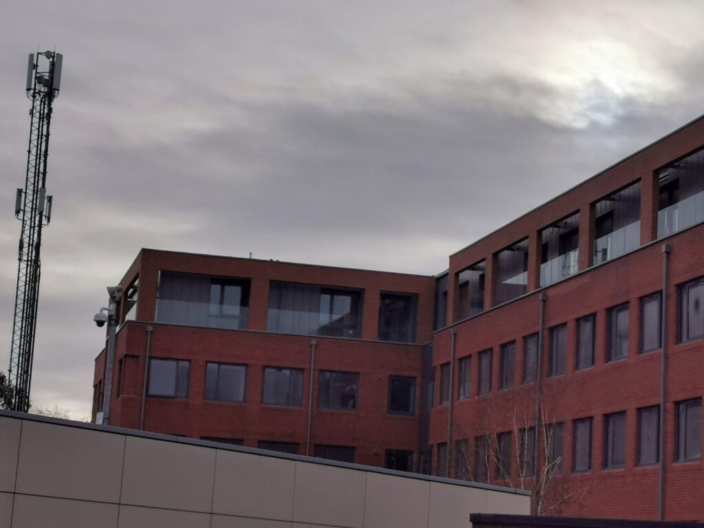Modern brick building with antennas under cloudy sky.