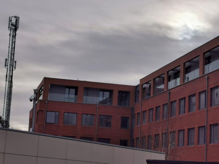 Modern brick building with antennas under cloudy sky.