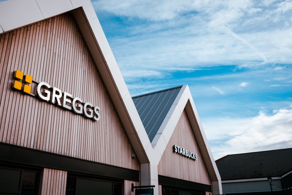 Greggs and Starbucks store signs under a blue sky